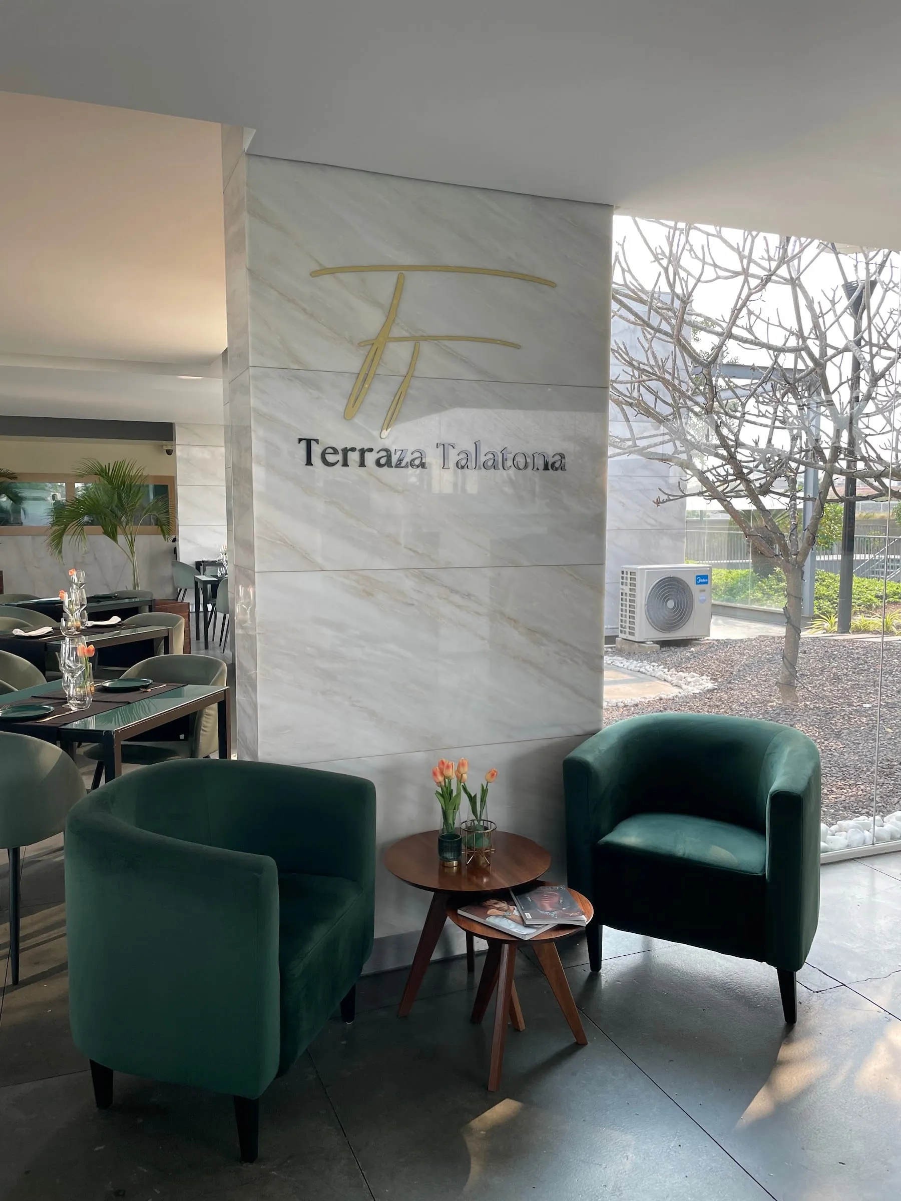 Zona lounge com poltronas verdes em frente à parede de mármore com o logótipo