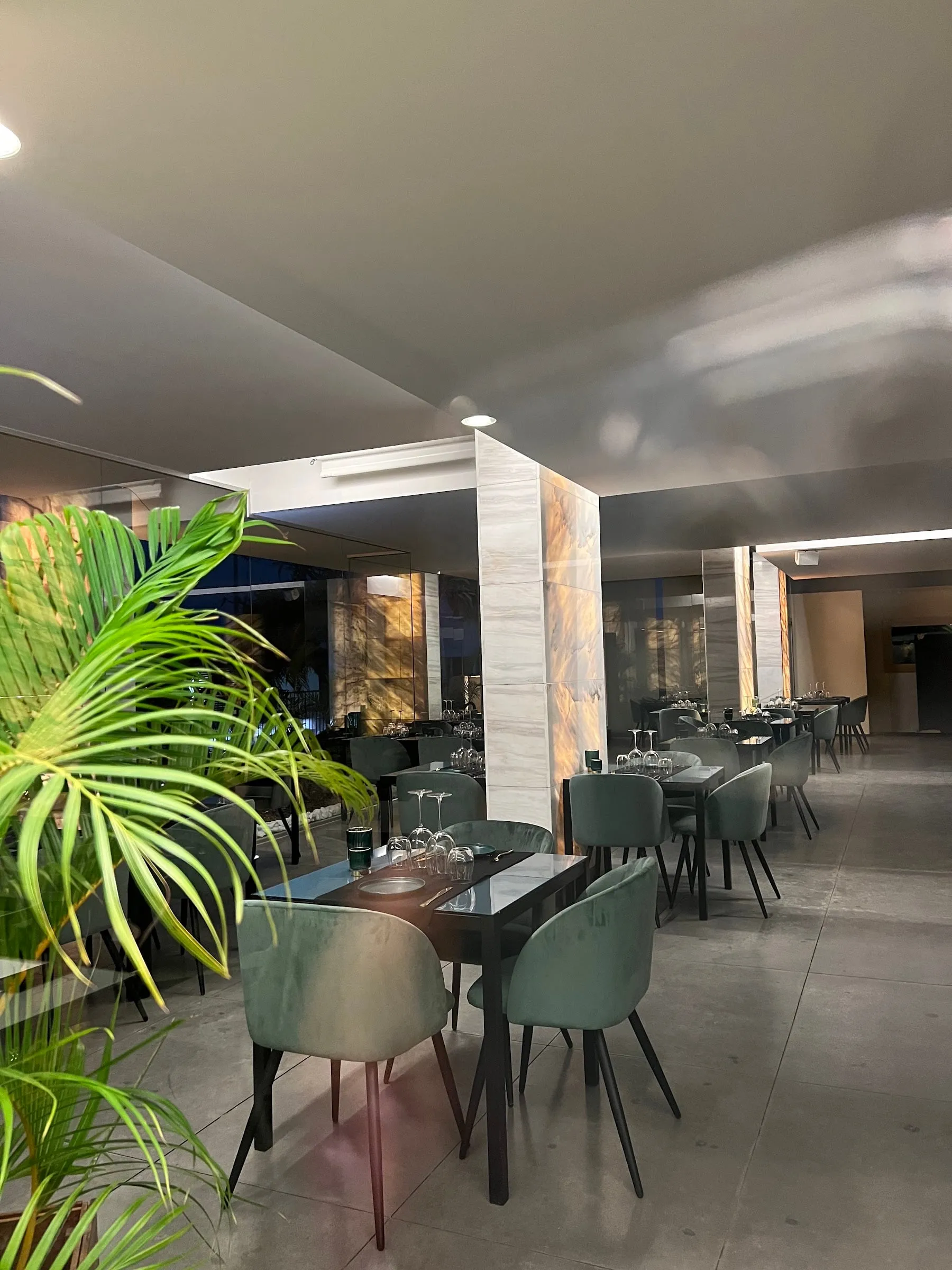 Sala interior com cadeiras verdes, colunas de mármore iluminadas e uma palmeira